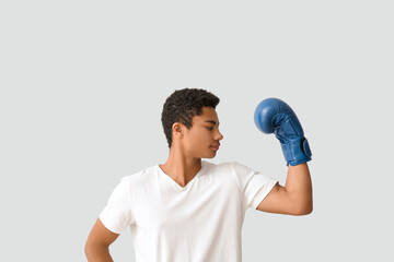 Young African-American man with boxing glove on light background. Immunity concept