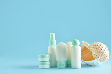 Travel bottles, jars with cosmetic products and sea shell on blue background