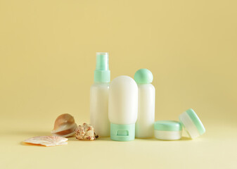 Travel bottles, jars with cosmetic products and sea shells on beige background