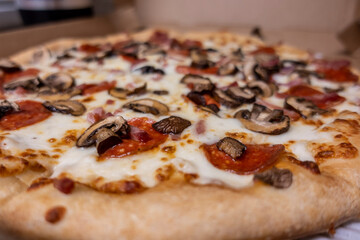 Macro, selective focus on a cheesy delivery pizza, topped with fresh mushrooms and pepperoni inside a cardboard box