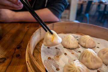 Close up view of a man picking up xiao long bao from a steamer basket inside a restaurant