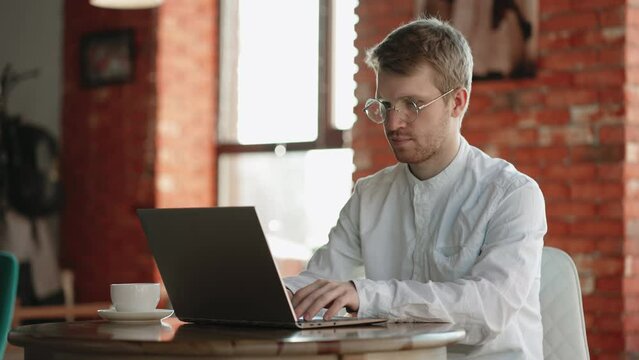 freelancer is working with laptop in cozy cafe in daytime, programmer or it specialist, using wireless internet connection