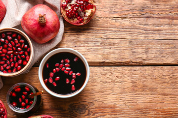 Jar and bowls of pomegranate molasses with fresh fruits on wooden background