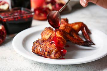 Pouring of pomegranate molasses onto roasted chicken wings on light background