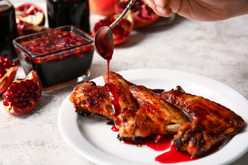 Woman pouring pomegranate molasses onto roasted chicken wings on light background