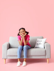 Obraz premium African-American teenage girl sitting on sofa against pink background