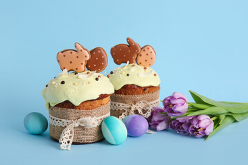 Obraz na płótnie Canvas Delicious Easter cakes decorated with cookies, flowers and painted eggs on blue background