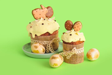 Delicious Easter cakes decorated with cookies and painted eggs on green background