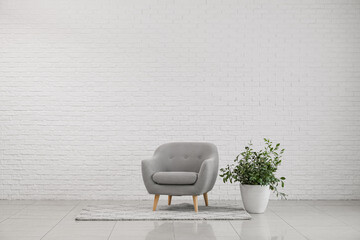 Modern armchair with houseplant near white brick wall
