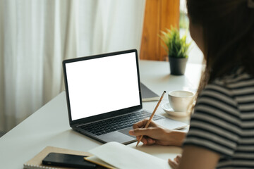 Young woman work on laptop with blank display screen with mockup copy space. Modern home living room interior design. Work at home concept.