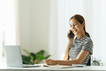 Happy charming woman using smartphone while working with laptop at home