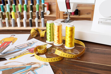 Thread spools with measuring tape, eyeglasses and sketches on table in atelier, closeup