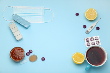 Frame made of medications for sore throat, tea cup, lemons, jam and thermometer on blue background