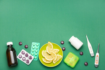 Plate with lemon slices, pills, syrup for sore throat and thermometers on green background