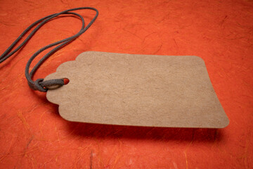 blank paper price tag with a twine against orange textured handmade paper, shopping concept