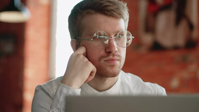 writer or journalist is sitting in cafe with laptop, portrait of pensive face with glasses, freelancer is working