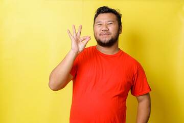 Asian young fat man with pouted lips showing gourmet sign with fingers tasty delicious isolated on yellow  background