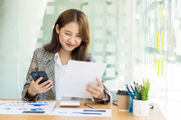 Business Startup Asian woman working with smartphone and graph document with laptop calculator to do analytical calculations. Finance and about real estate investment costs and tax systems.