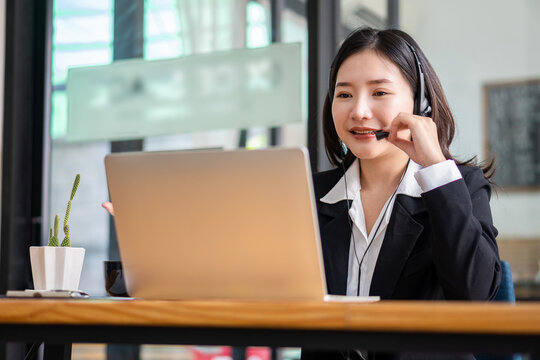 Female manager of Asian ethnicity who is happy in headphones looking at laptop screen. Chat happily with customers online. work remotely in the workplace education concept work-study at a coffee shop