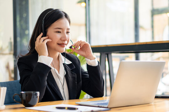 Female manager of Asian ethnicity who is happy in headphones looking at laptop screen. Chat happily with customers online. work remotely in the workplace education concept work-study at a coffee shop