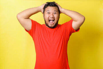 Fototapeta na wymiar Attractive young Asian fat man in red t-shirt with shiny teeth, shouting, touching head, isolated over yellow background