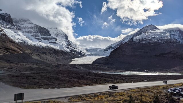 Admiring the view of the Athabasca Ice Glacier from across the road near dusk. The sun is about to set, the clouds are rolling around the peaks, and a truck is on its way home on an empty road.