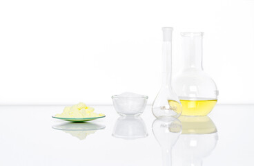 Sulfur Powder in Chemical Watch Glass place next to White flake chemical in glass container, Volumetric flask and Aluminium chloride liquid in Flat Bottom Flask.  Side View