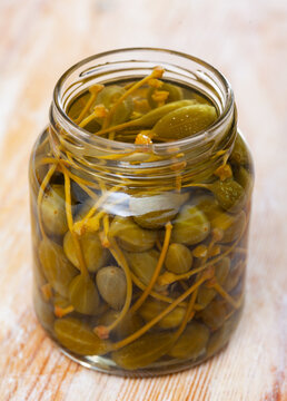 Closeup of glass jar with pickled green capers on a wooden background