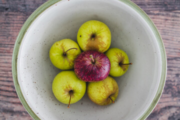 group of green apples with one red apple in the middle, healthy food or metaphor of standing out from the crowd