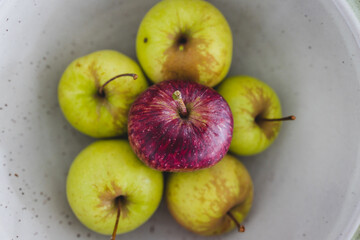 group of green apples with one red apple in the middle, healthy food or metaphor of standing out from the crowd