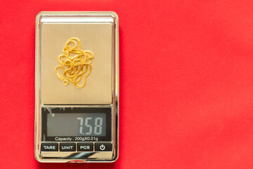 Gold necklace weigh on digital electronic scale and red velvet background