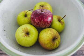 group of green apples with one red apple in the middle, healthy food or metaphor of standing out from the crowd