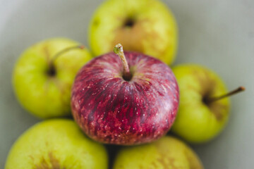 group of green apples with one red apple in the middle, healthy food or metaphor of standing out from the crowd