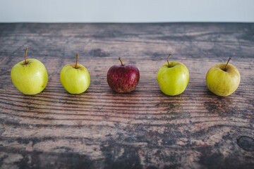 group of green apples with one red apple in the middle, healthy food or metaphor of standing out from the crowd