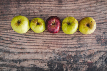 group of green apples with one red apple in the middle, healthy food or metaphor of standing out from the crowd
