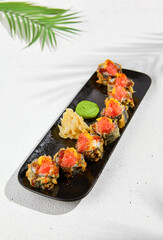 Tempura sushi roll with grapefruit and mango sauce. Hot maki sushi in black plate on white background. Summer menu for japanese restaurant. Modern sushi menu with hard shadow and leaves.