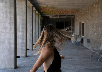 Portrait of a young woman  wearing a black dress, shaking her hair in the concrete gallery. 