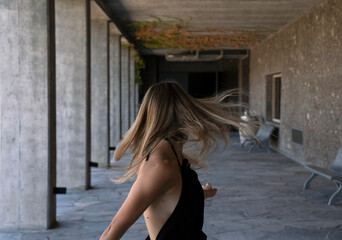 Naklejka premium Portrait of a young woman wearing a black dress, shaking her hair in the concrete gallery. 