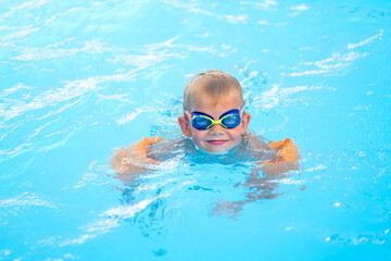 Portrait smiling boy in swimming pool, child in swimming glasses and inflatable sleeves. Summer...