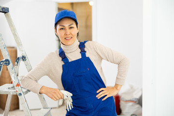 Portrait of positive Asian woman builder standing in apartment.