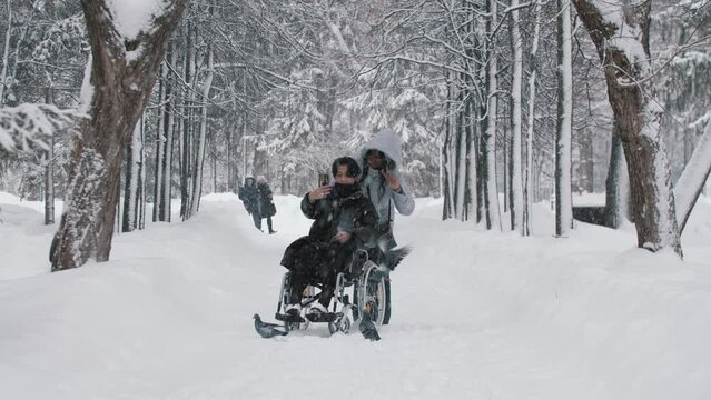Young couple of asian guy in the wheelchair and his black girlfriend taking a selfie in winter forest