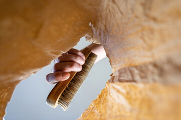 A hand places a clothes brush in a paper bag. A mature man's hand holds the brush with a wooden handle over the open brown bag. Shot from the bottom up. Close up. Selective focus