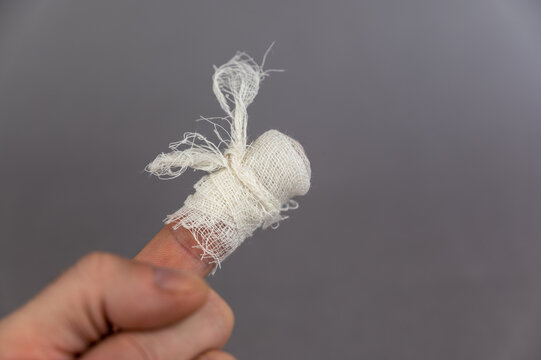 The hand of a mature man with a bandaged index finger. The man holds his palm against the gray background. Health and Medicine.