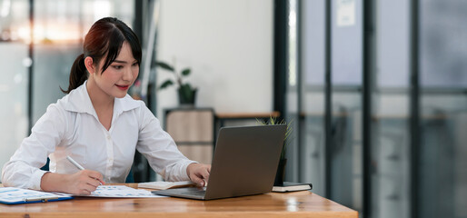 Young asian beautiful and charming businesswoman smiling and working on laptop computer at office.