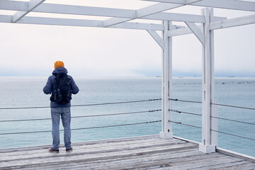 A man in winter clothes by the sea looks into the distance. The concept of travel, winter holidays. Front view.