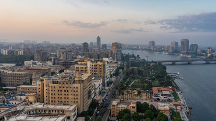 View of Cairo from a height. The Nile skirts an urban area with many buildings.  A bridge over the river is visible. Lilac clouds in the evening pinkish sky. Egypt