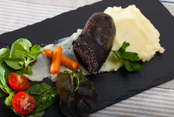 Blood sausage served on slate plate with pureed potatoes, vegetables and herbs