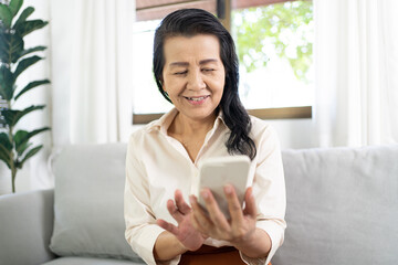 Middle age Asian woman holding cell telephone Work from home. smiling Beautiful mature asian woman VDO Call Conference smart phone with technology concept