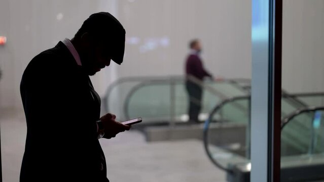 dark silhouette of african man with smartphone against metro entrance in city, townsman is waiting someone