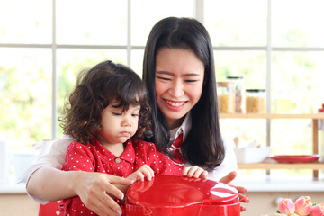Happy smiling beautiful young mom with her little adorable child daughter girl opening surprise red...